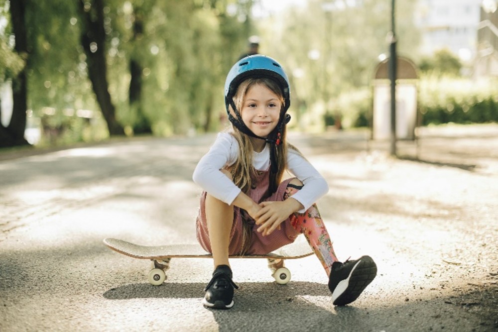 Young girl with a prosthetic leg sitting on a skateboard.