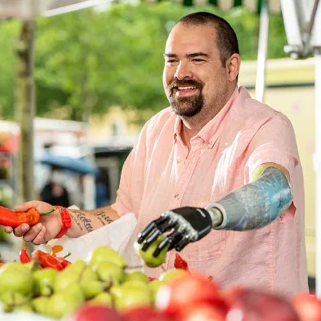 A man with an i-Digits® Quantum prosthetic arm holds a fruit in New York, New Jersey, & Connecticut